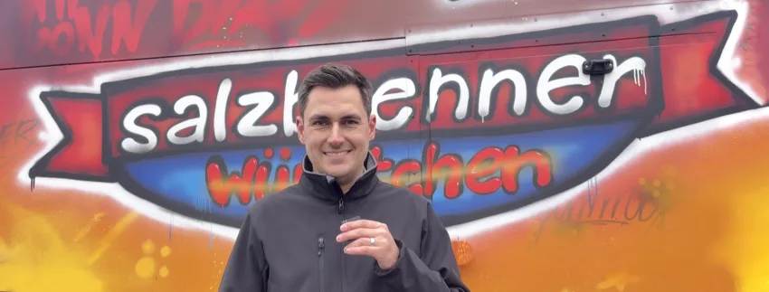 Leif Holst steht vor farbigem Graffiti mit Schriftzug „salzbrenner Würstchen“ als Symbolbild für Praxisbezug in SAP Business One