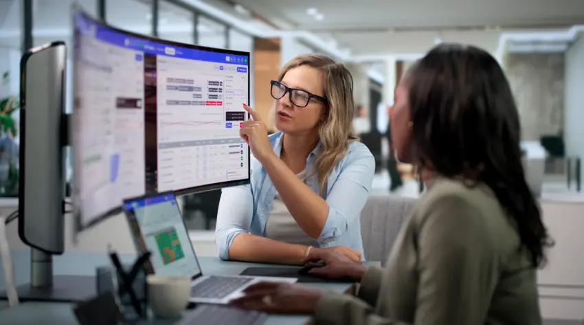 Zwei Mitarbeiterinnen besprechen Daten und Auswertungen auf einem großen Bildschirm im Büro.